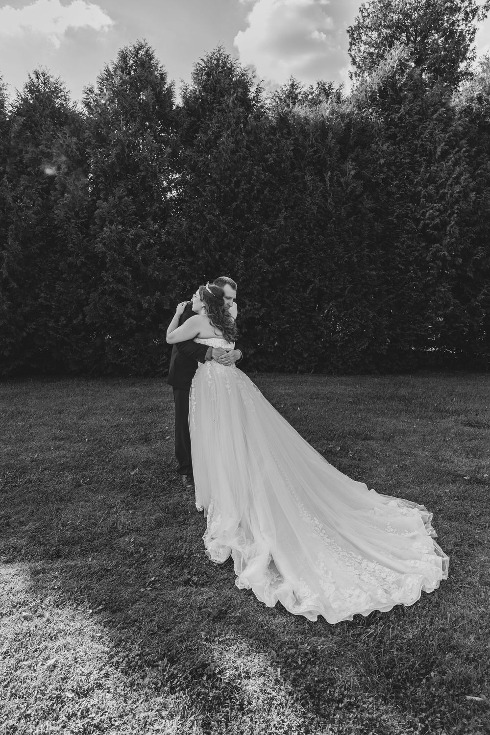 A flowing white wedding dress train spreads elegantly across a grassy field during their father/daughter first look in Sheboygan WI with ERP