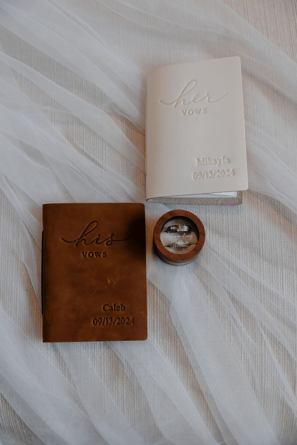 Wedding vow books and rings arranged on white fabric with elegant lettering in Milwaukee, WI  with Essence Rose Photography.
