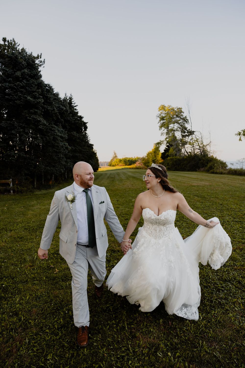 A couple in wedding attire walks hand in hand across a grassy hillside on their special day.