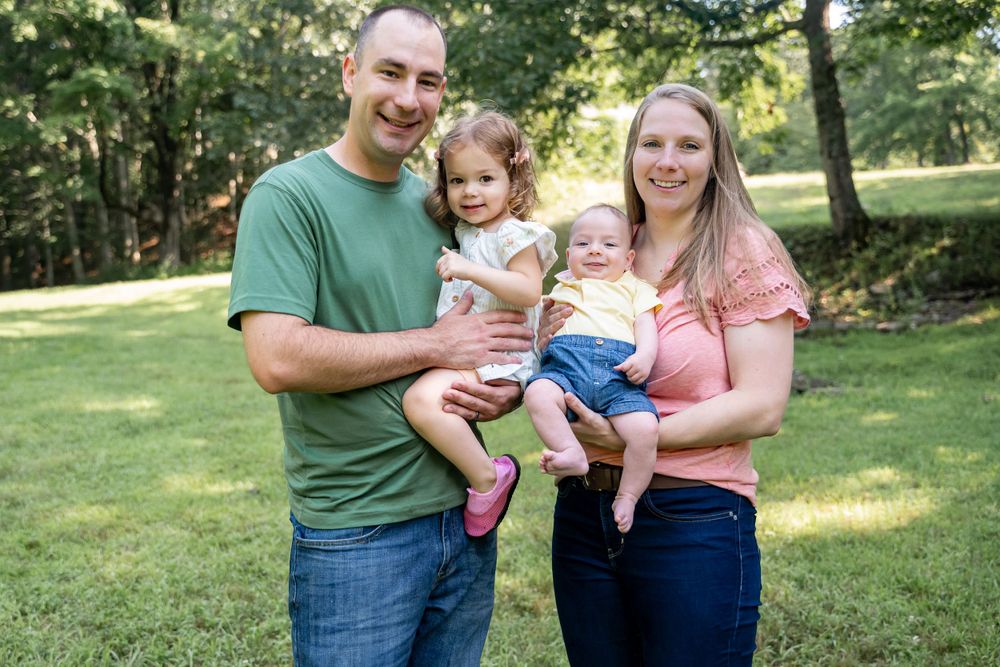 Family of four poses together on sunny lawn in casual summer attire.
