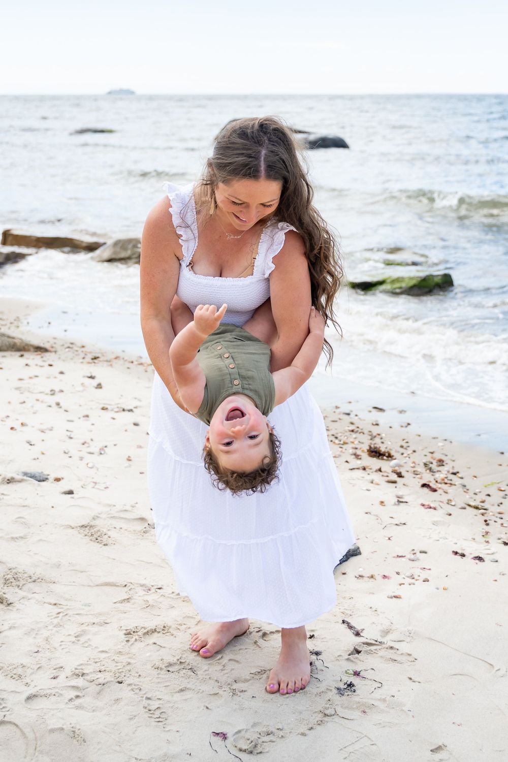Playful interactions between parent and child on a sandy beach with ocean waves in background.
