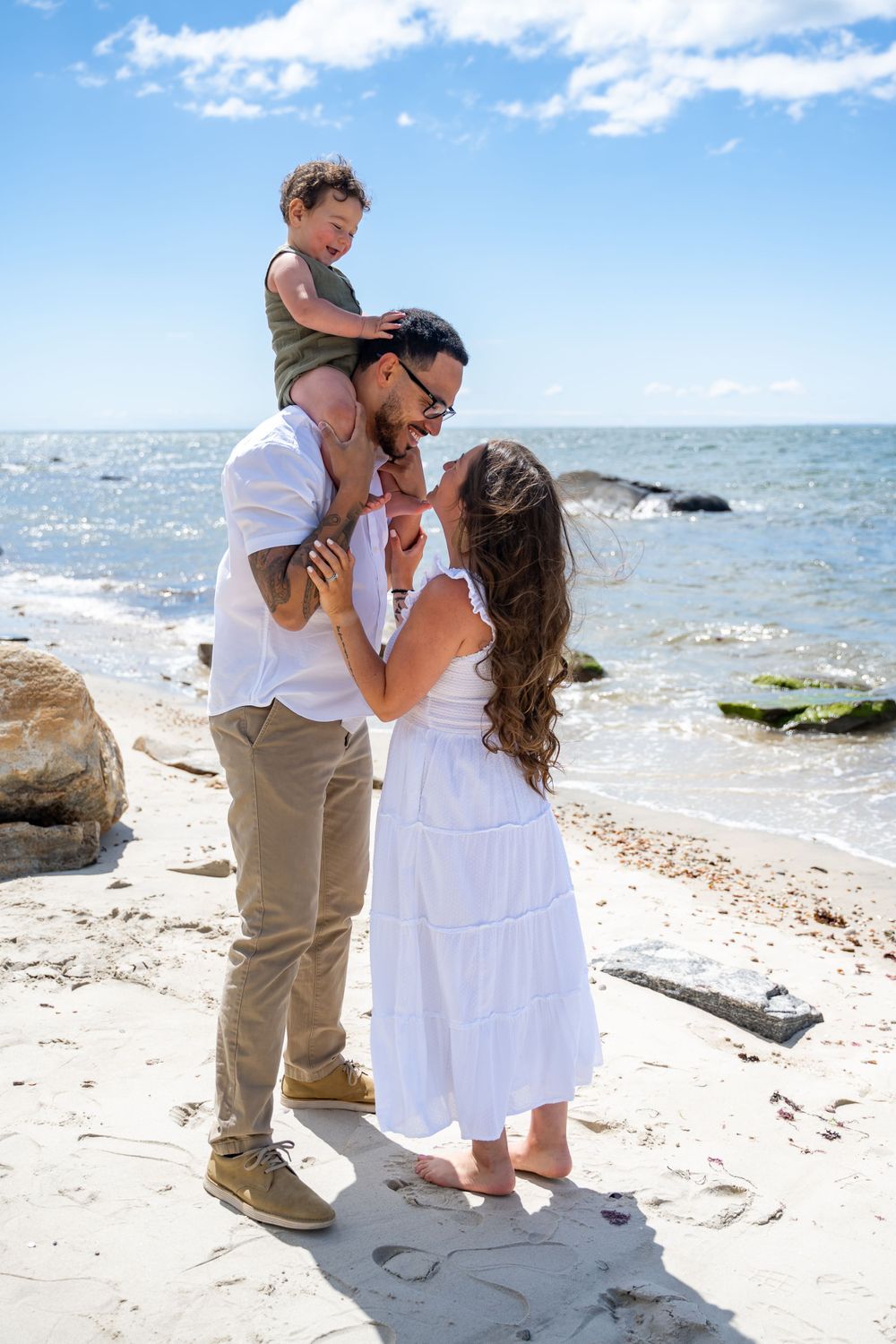 A family shares an intimate moment together on a beach with sparkling ocean waters behind them.