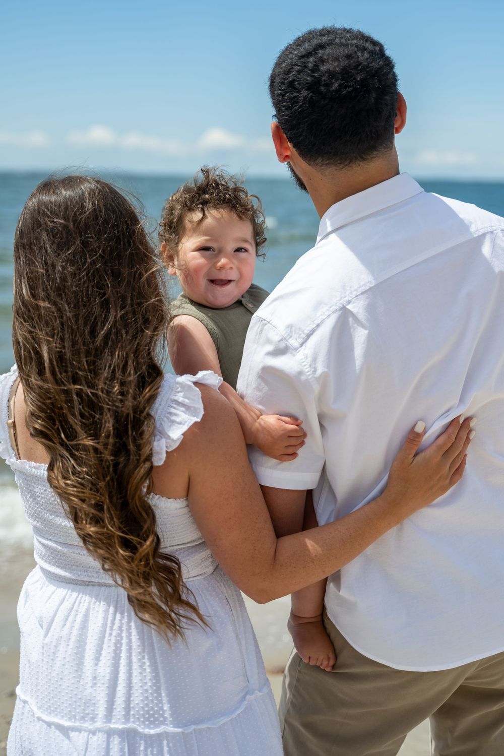 A family shares a tender moment together while standing on a sunny beach.