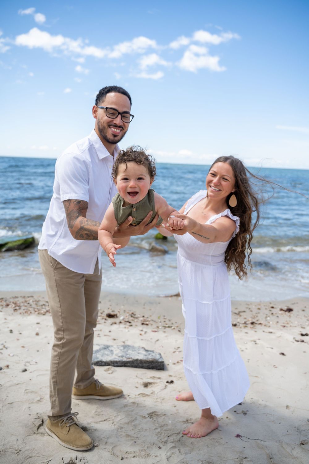 A playful family moment captured on a beach with bright blue skies and ocean in the background.