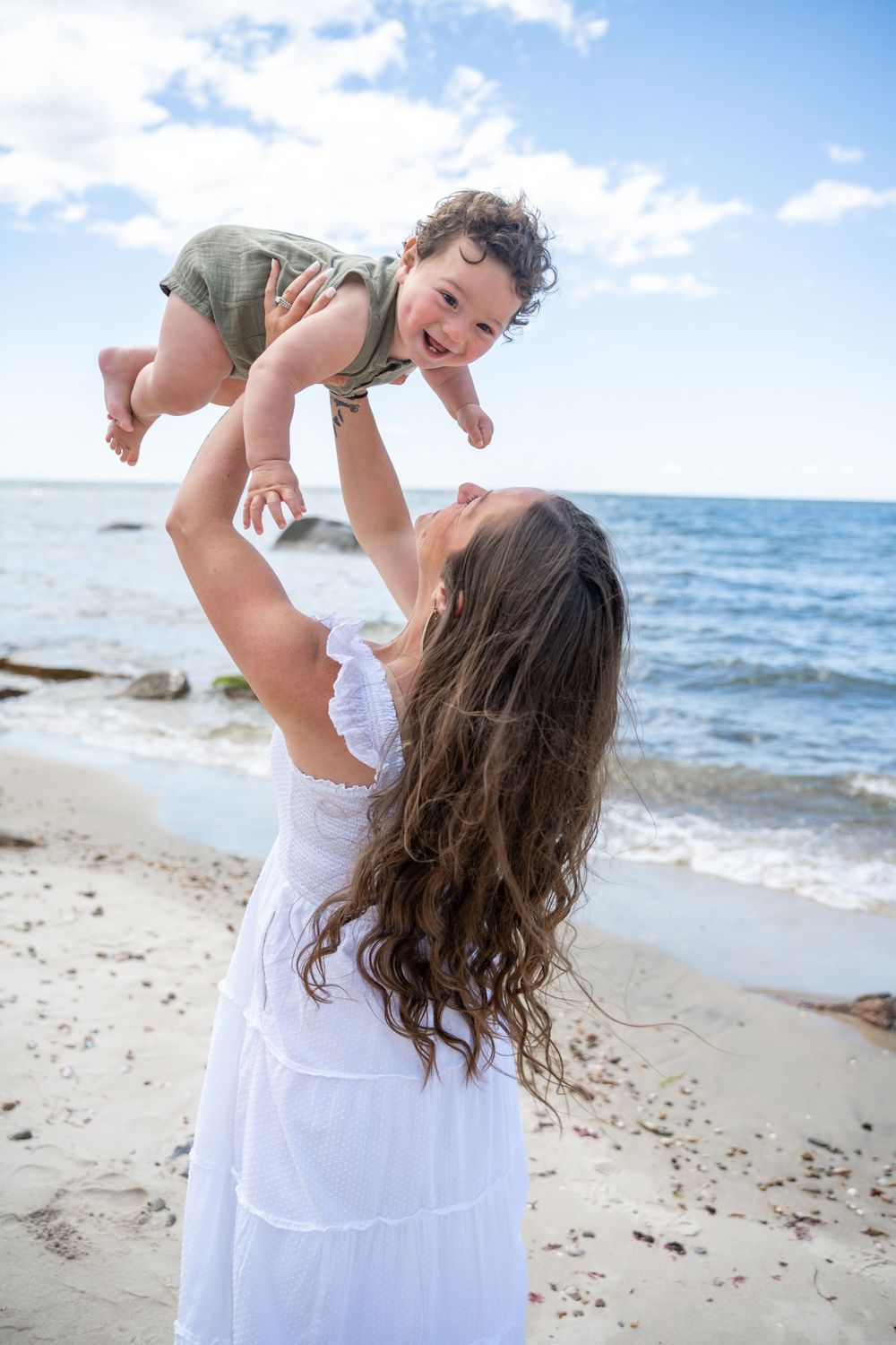 A joyful moment shows a person lifting a laughing toddler against a beautiful beach background.