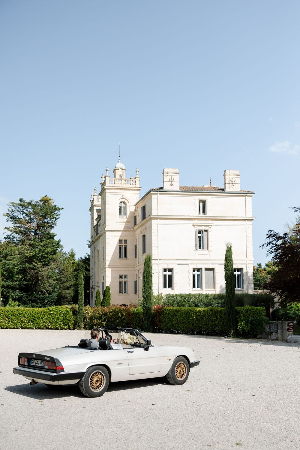 Classic white convertible car parked in front of an elegant white mansion estate.