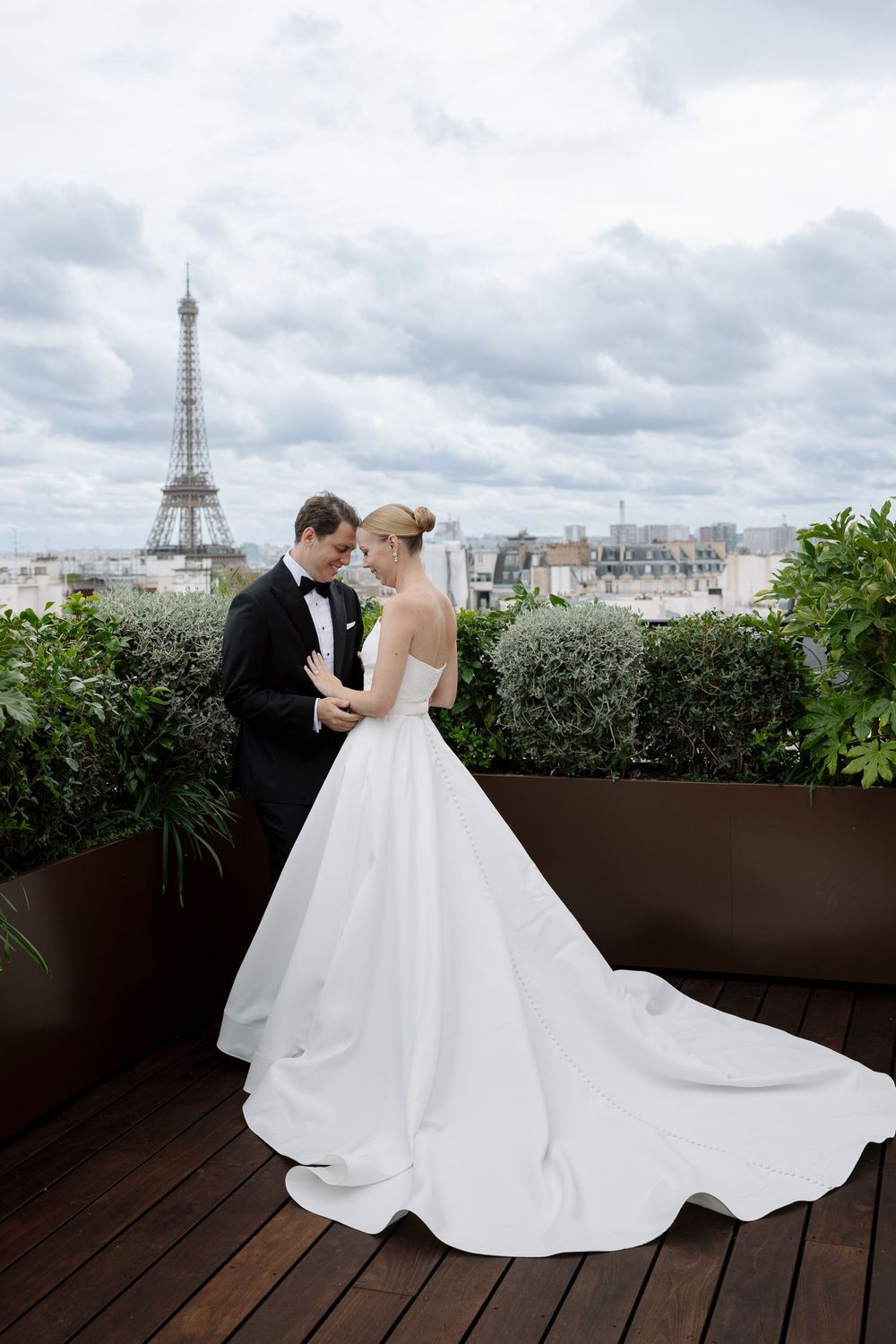 Romantic wedding photo on Paris rooftop with Eiffel Tower in cloudy background.