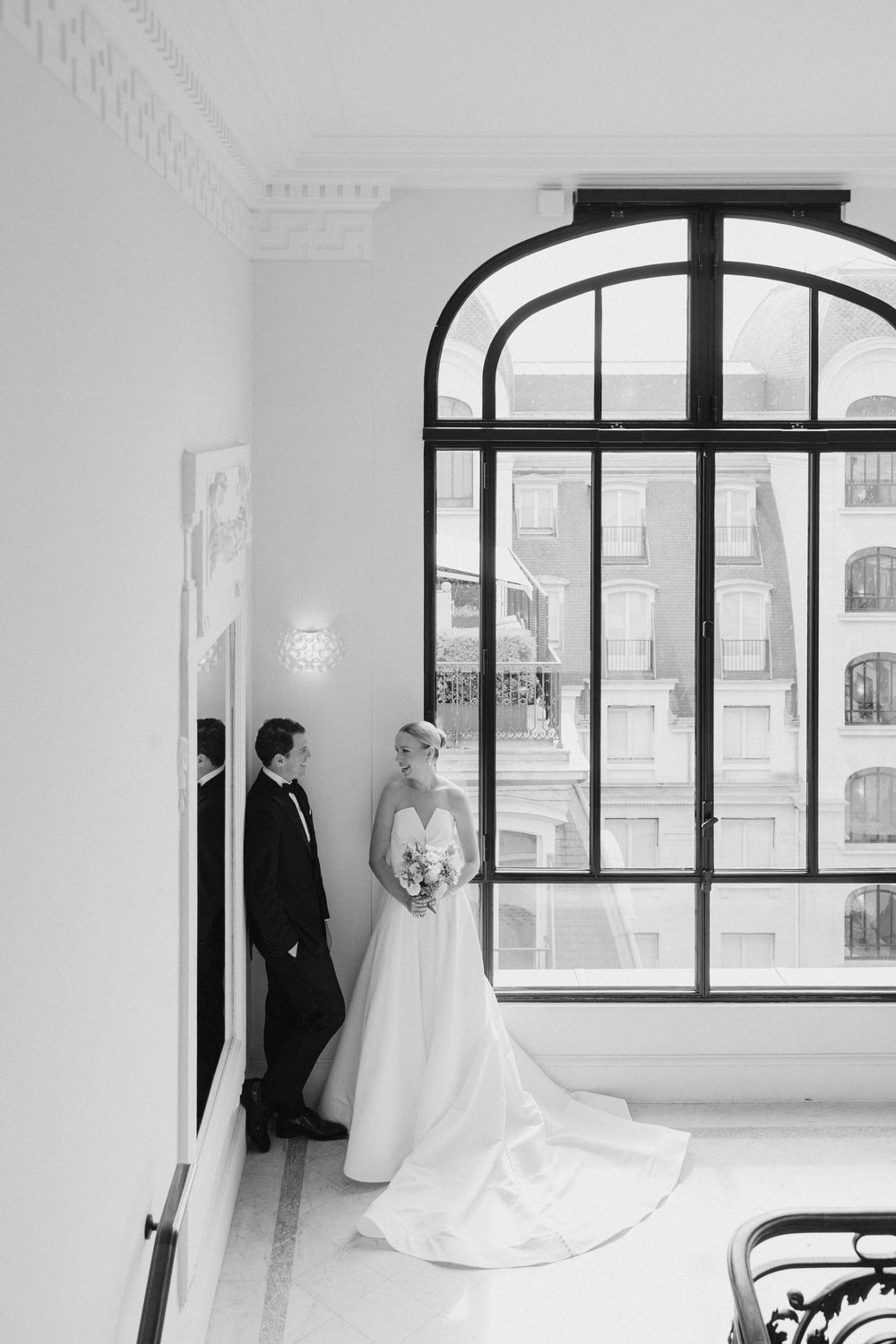 Elegant black and white wedding portrait by arched window in classic interior.