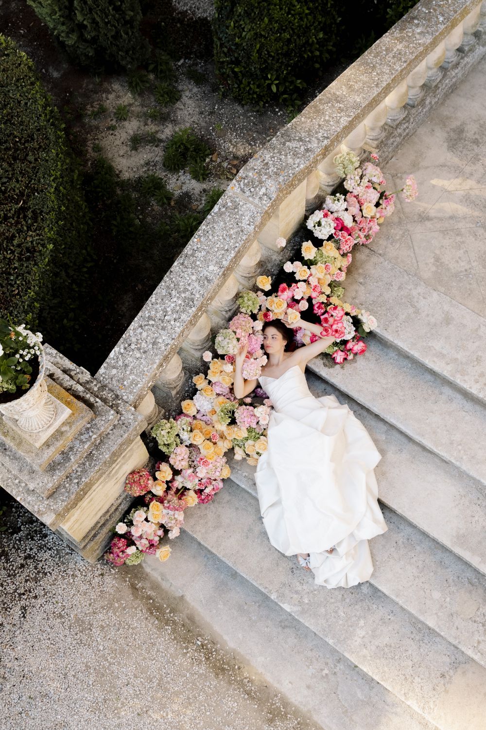 White wedding dress trailing down stone steps decorated with pink and peach flowers.