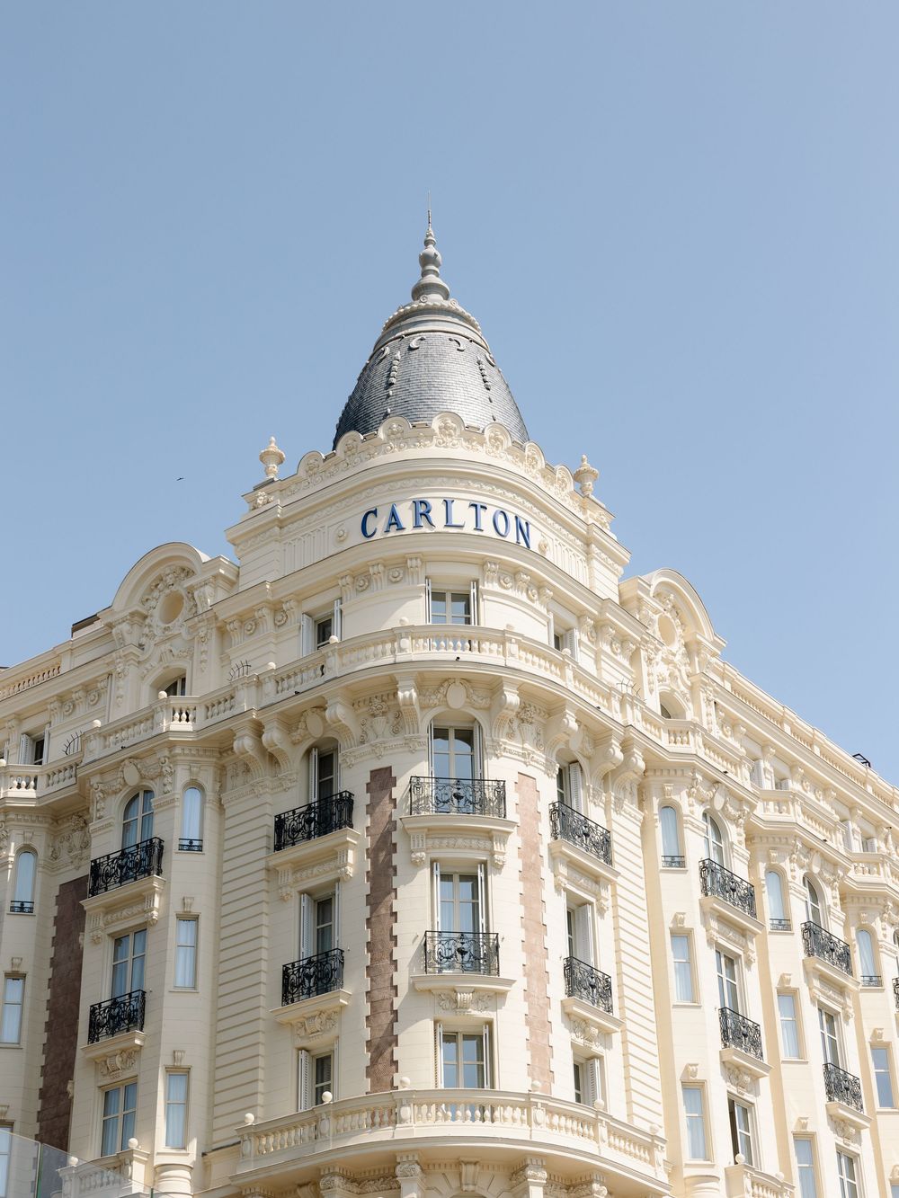 Elegant beige Carlton hotel facade with ornate architectural details and balconies against blue sky.