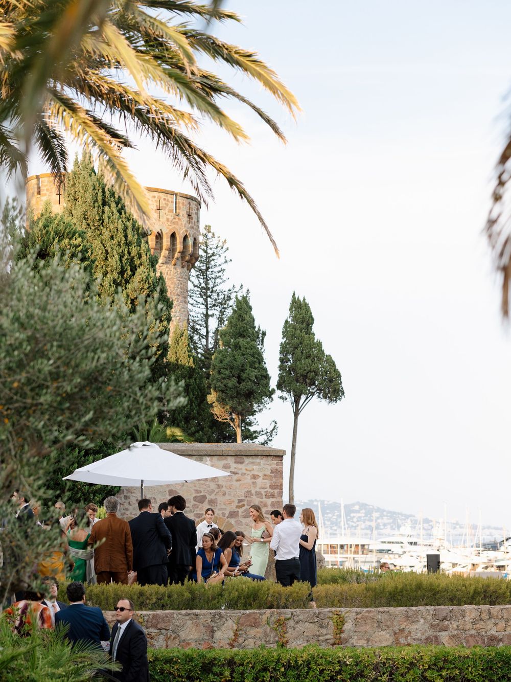 Palm trees and stone walls frame an outdoor gathering space with umbrellas.