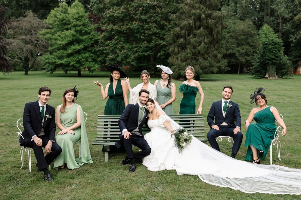 Wedding party relaxing on grass in formal attire with emerald green bridesmaid dresses.