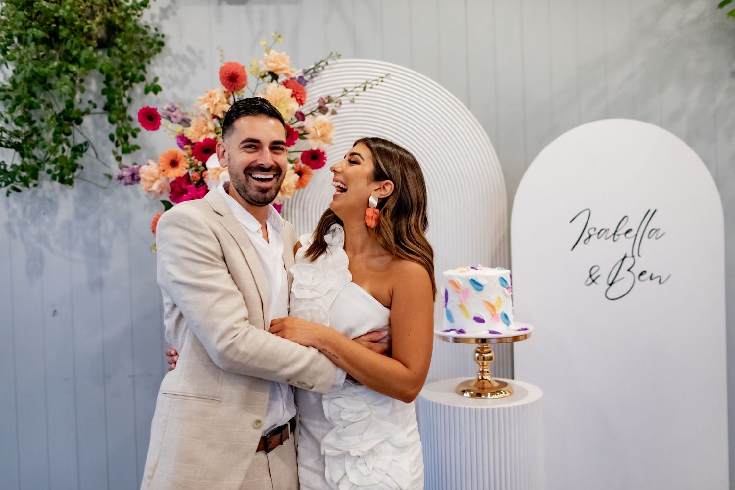 A joyful celebration moment against an elegant white arch backdrop with floral decorations.