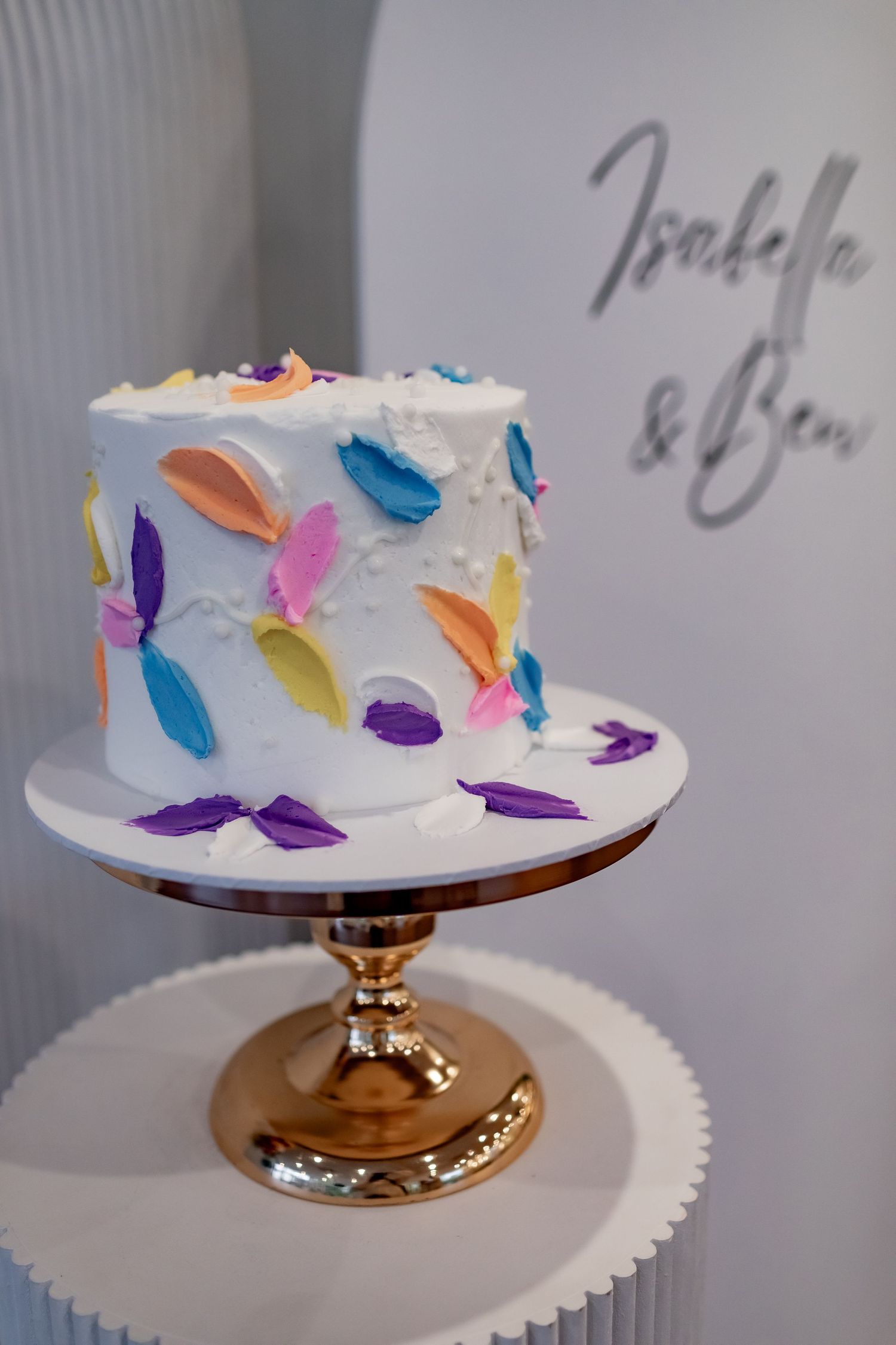 White wedding cake decorated with colorful butterfly designs on gold cake stand.