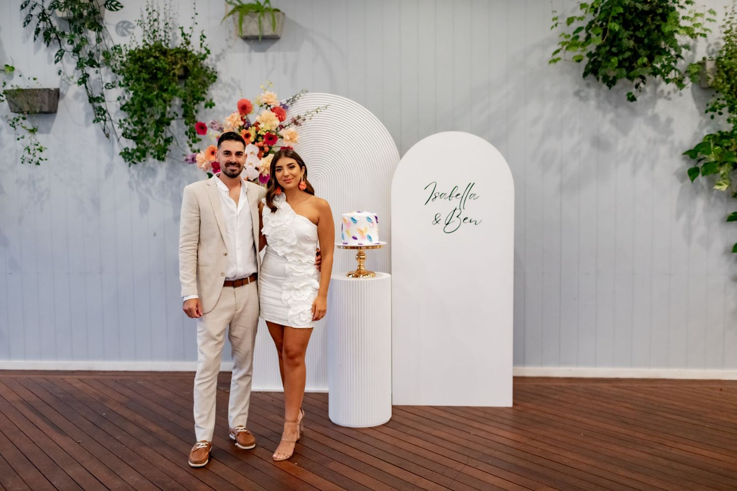 Engagement celebration setup with white arch backdrop and vibrant floral decorations.