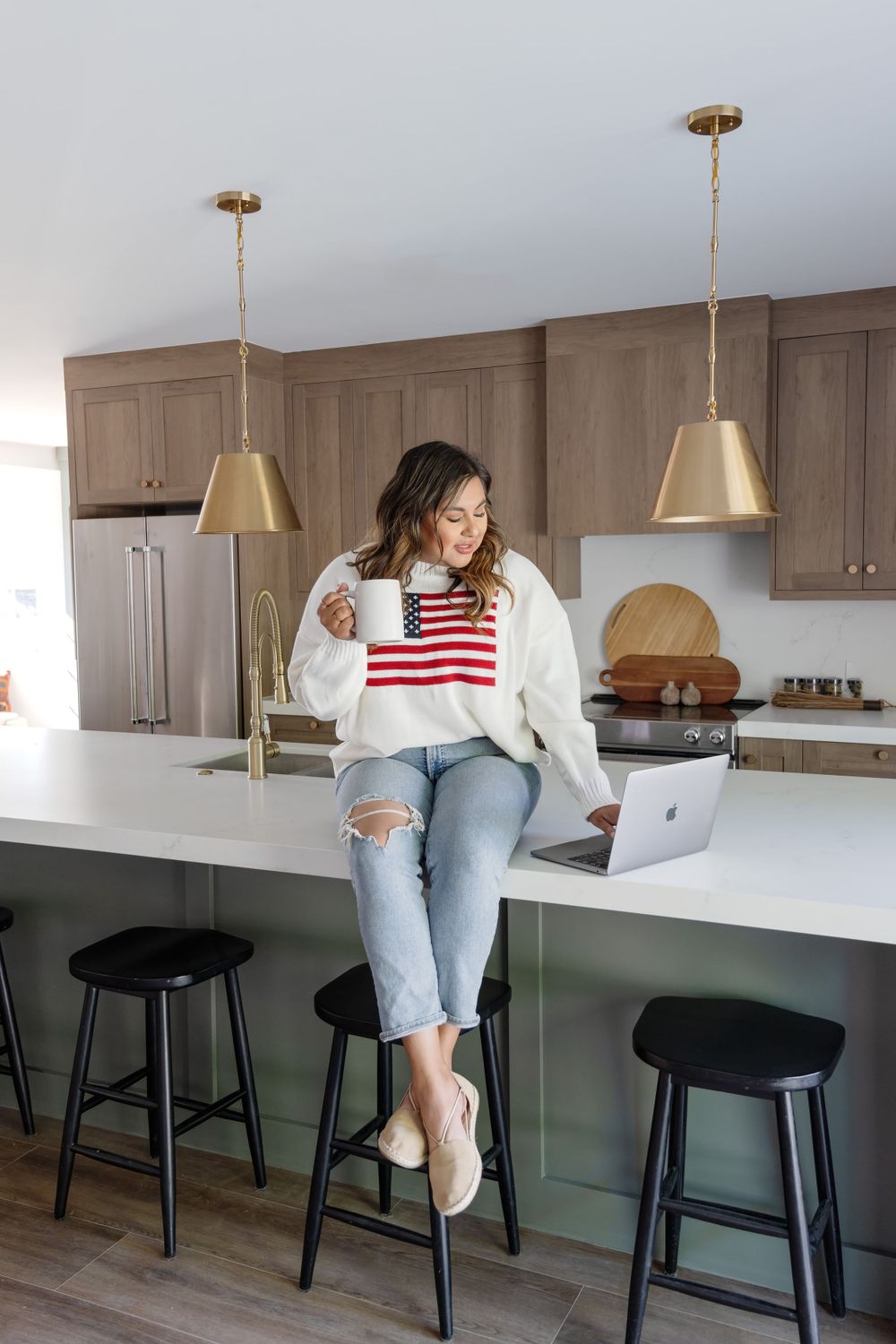 Modern kitchen featuring brass pendant lights and someone working on laptop at counter.