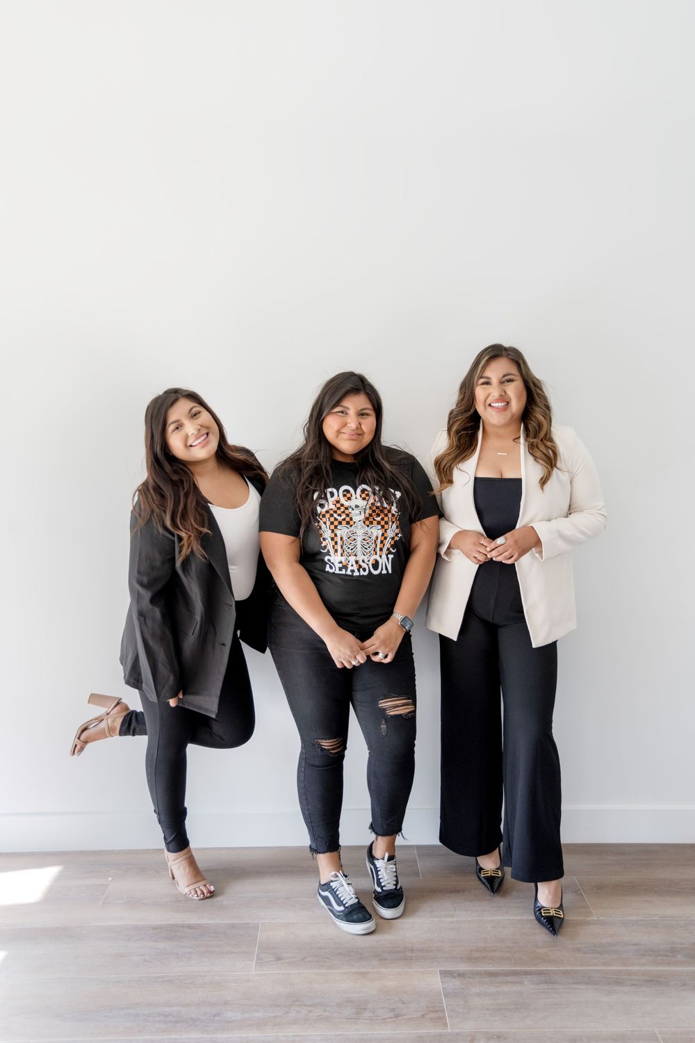 Group photo of three friends posing casually against white wall.