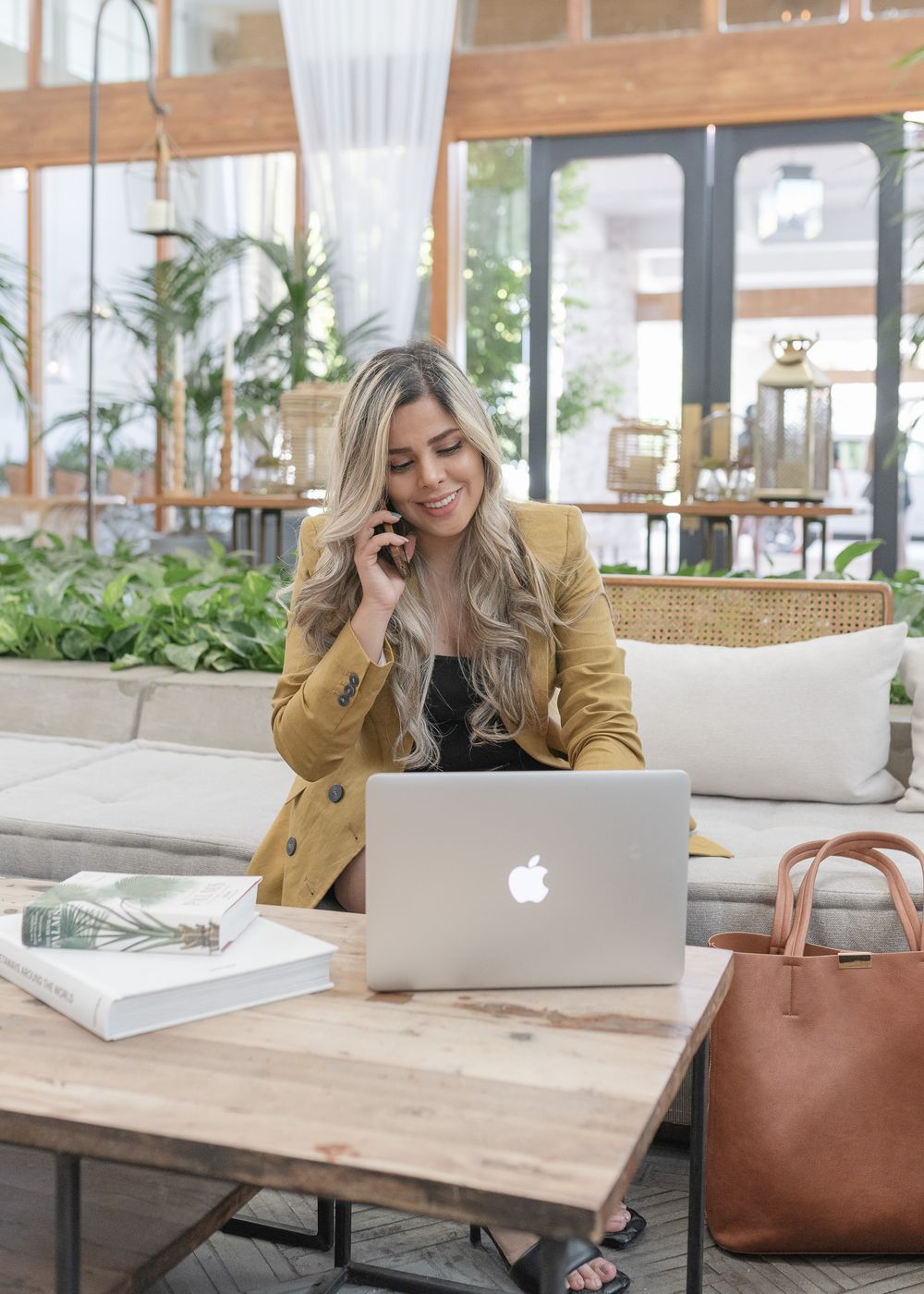 Modern workspace setting with laptop, leather bag and indoor plants in bright sunroom.