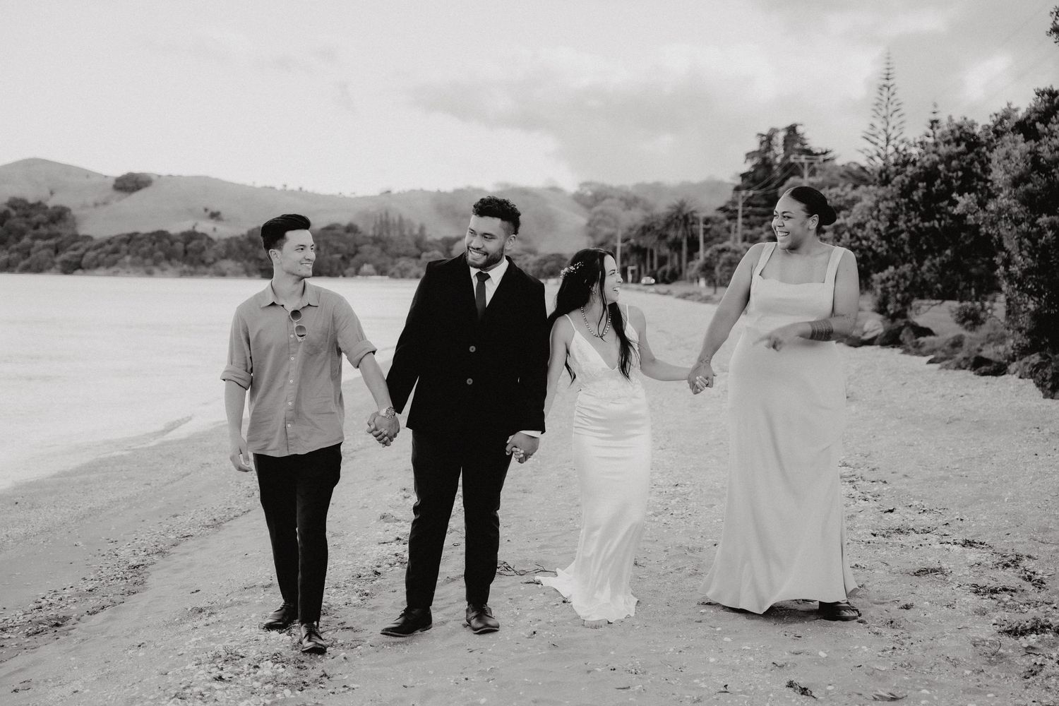 Four people walking along a beach shoreline in formal attire during a black and white photo session.