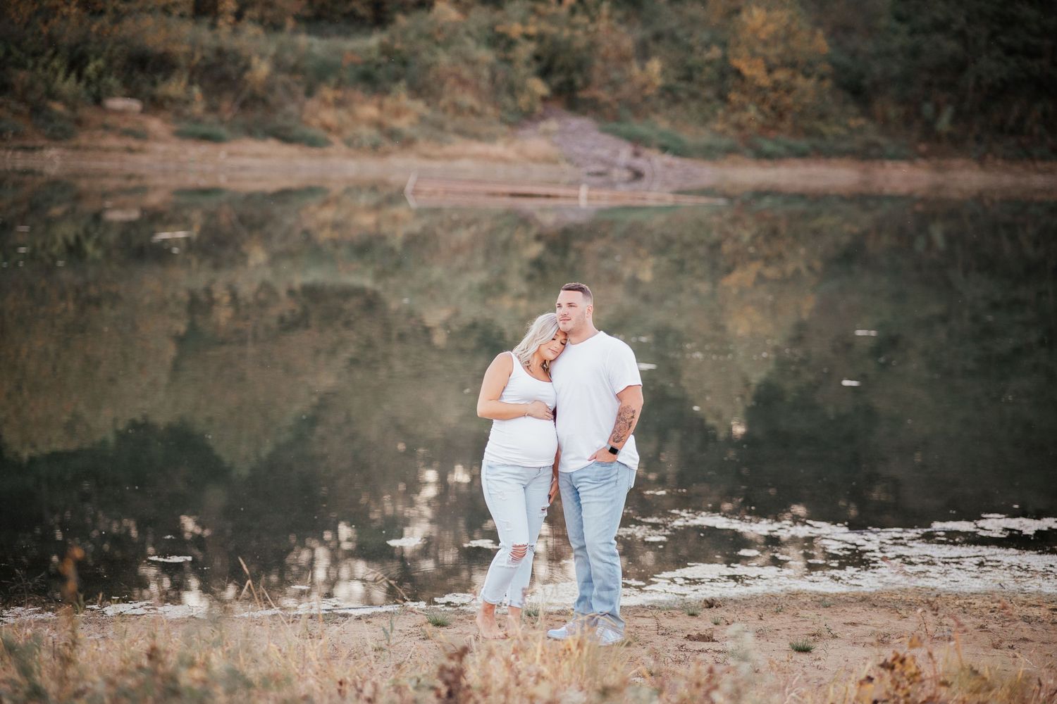 A couple embraces on a rocky outcrop overlooking a reflective pond.