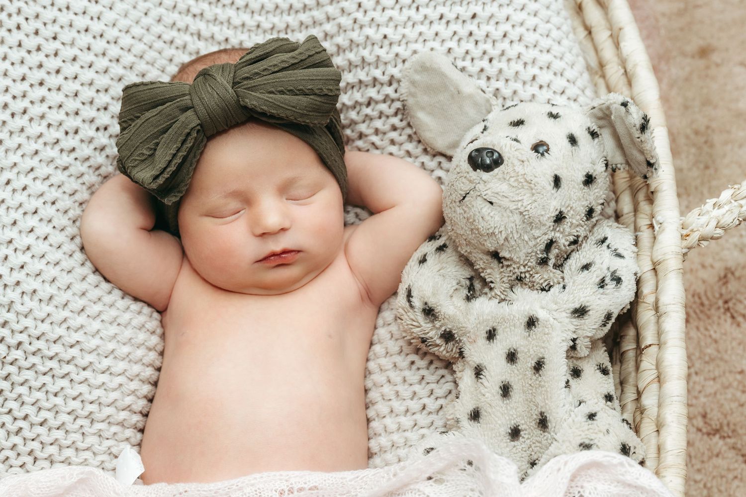 Newborn baby sleeping peacefully next to spotted plush toy on knit blanket.