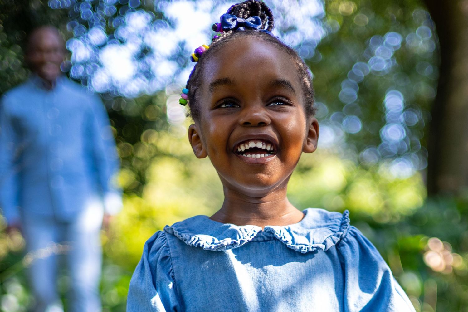 Joyful child in blue dress laughing outdoors in sunny garden setting.