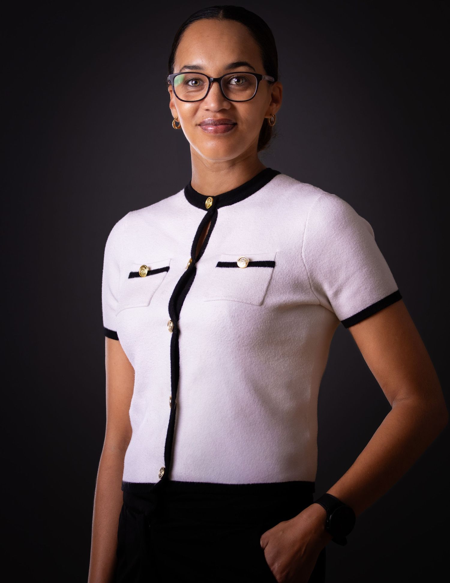 Professional studio portrait of someone wearing a white button-up shirt with black trim and glasses against dark background.