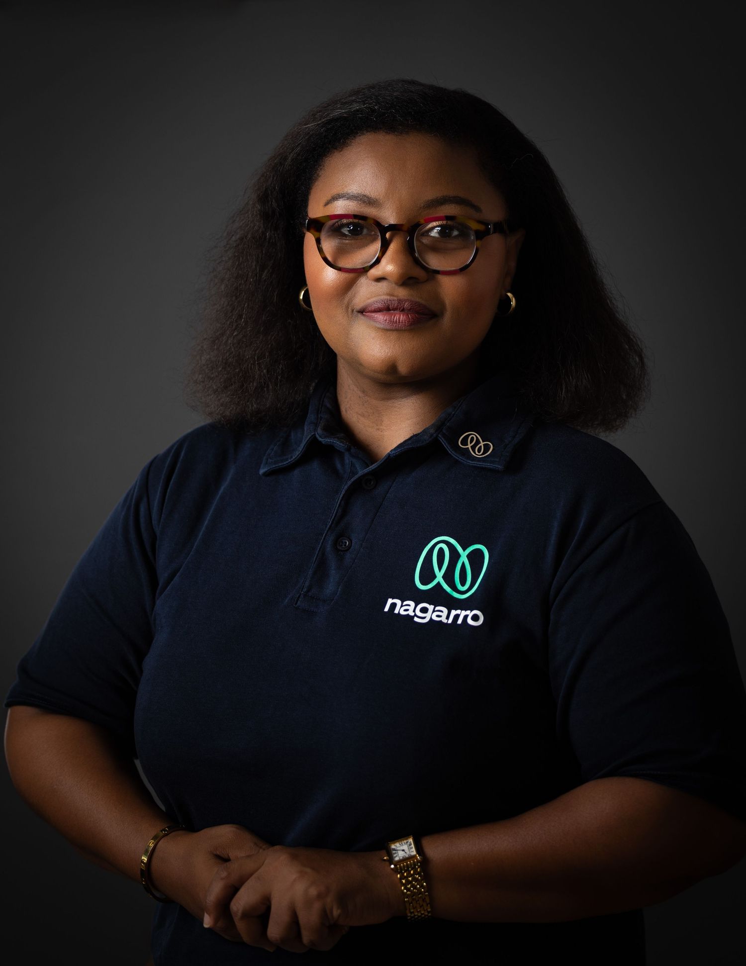 Professional corporate portrait of an employee wearing a navy blue polo shirt with company logo against dark background.