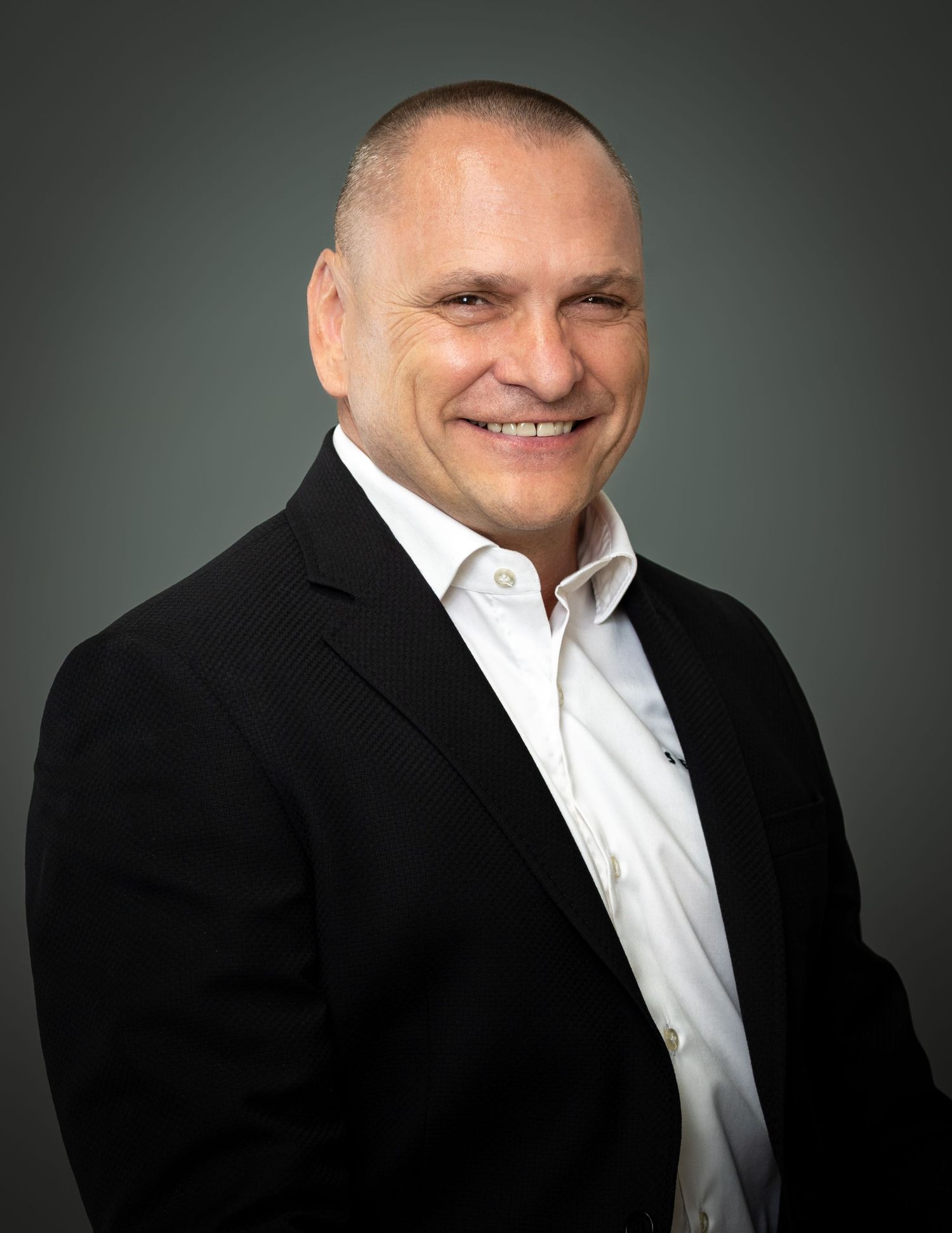 Professional portrait of man in business attire smiling against gray studio background.
