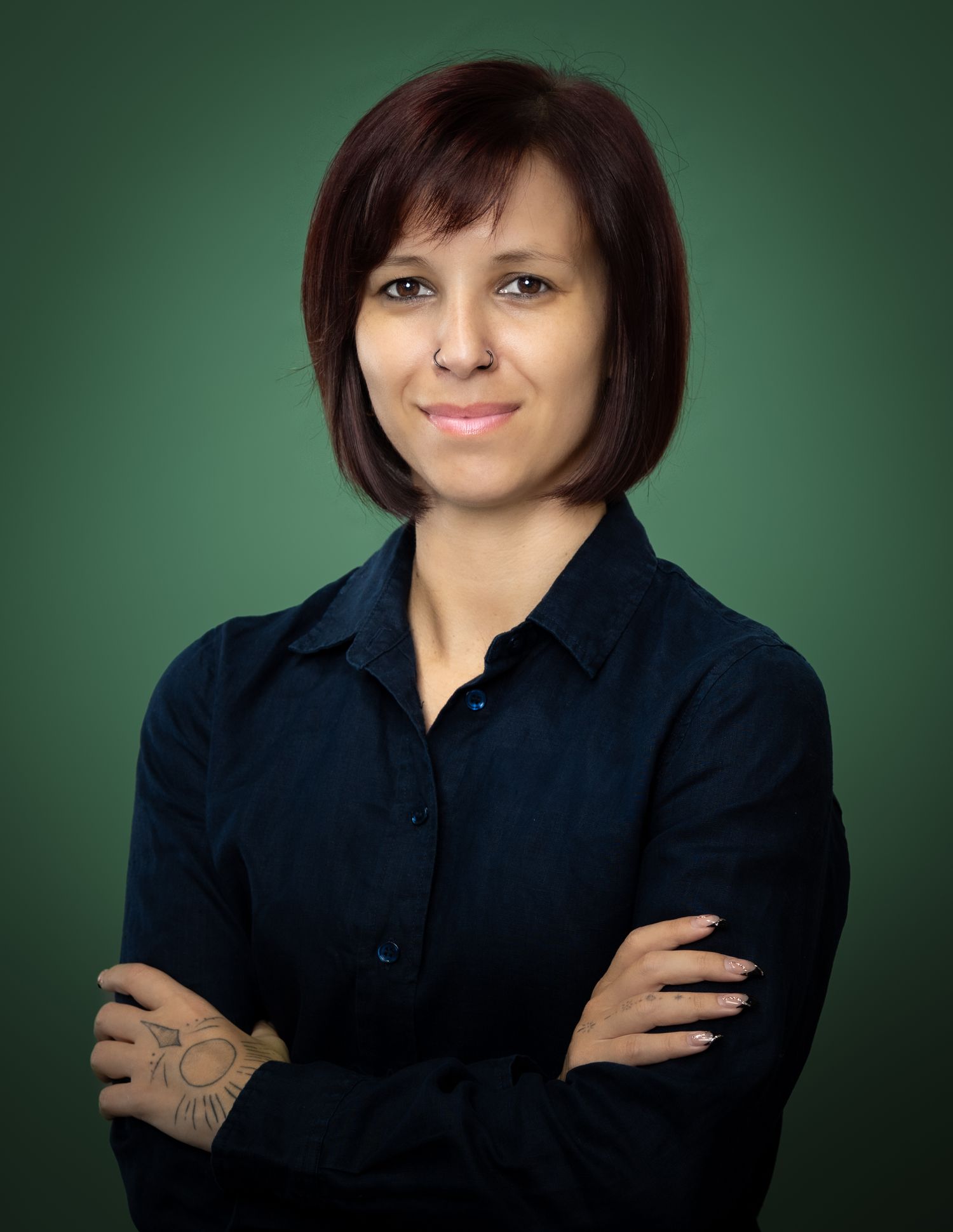 Professional portrait of someone in a navy blue button-down shirt against a green background, with arms crossed.