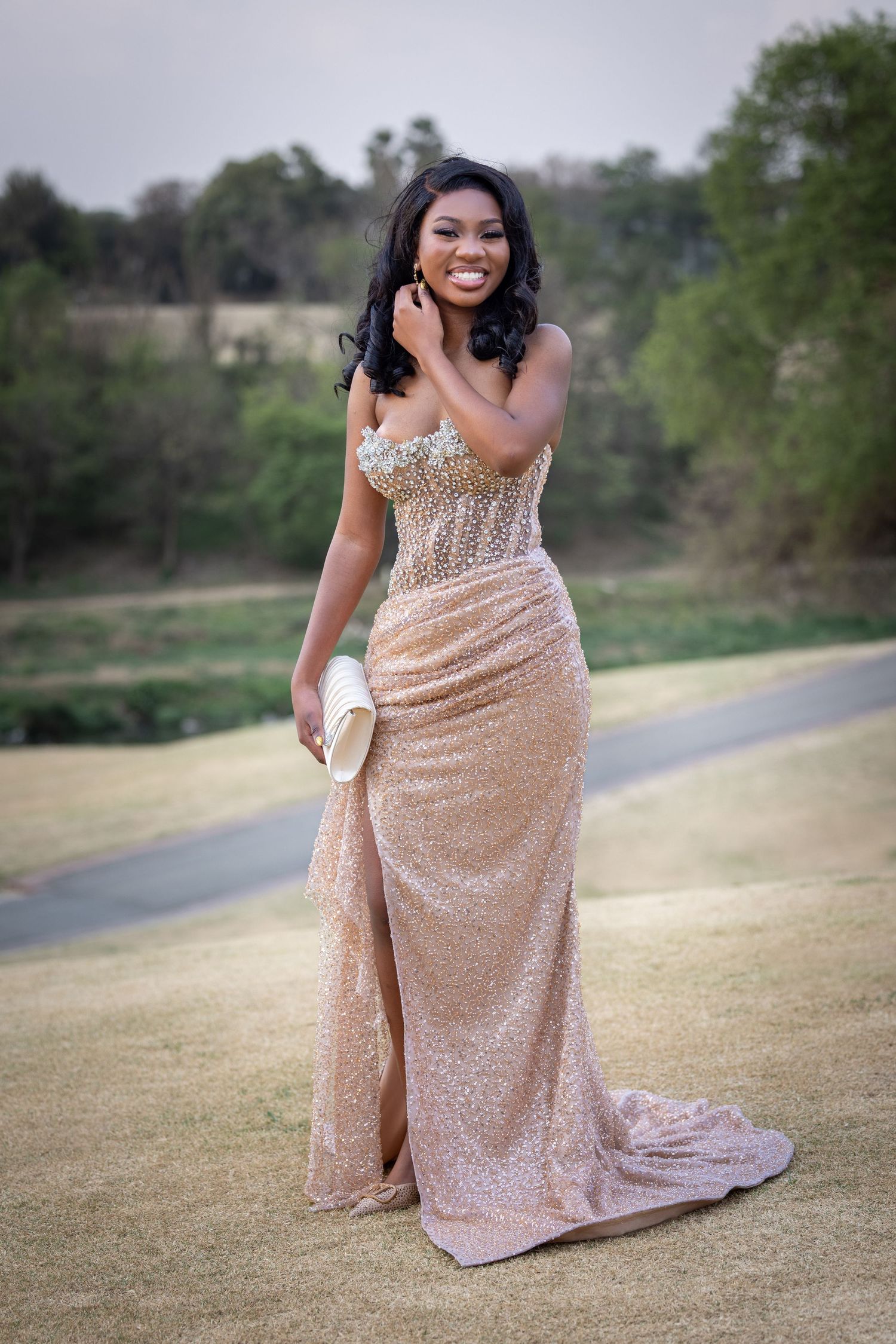 Person in a rose gold sequined gown poses gracefully on a grassy field at sunset.