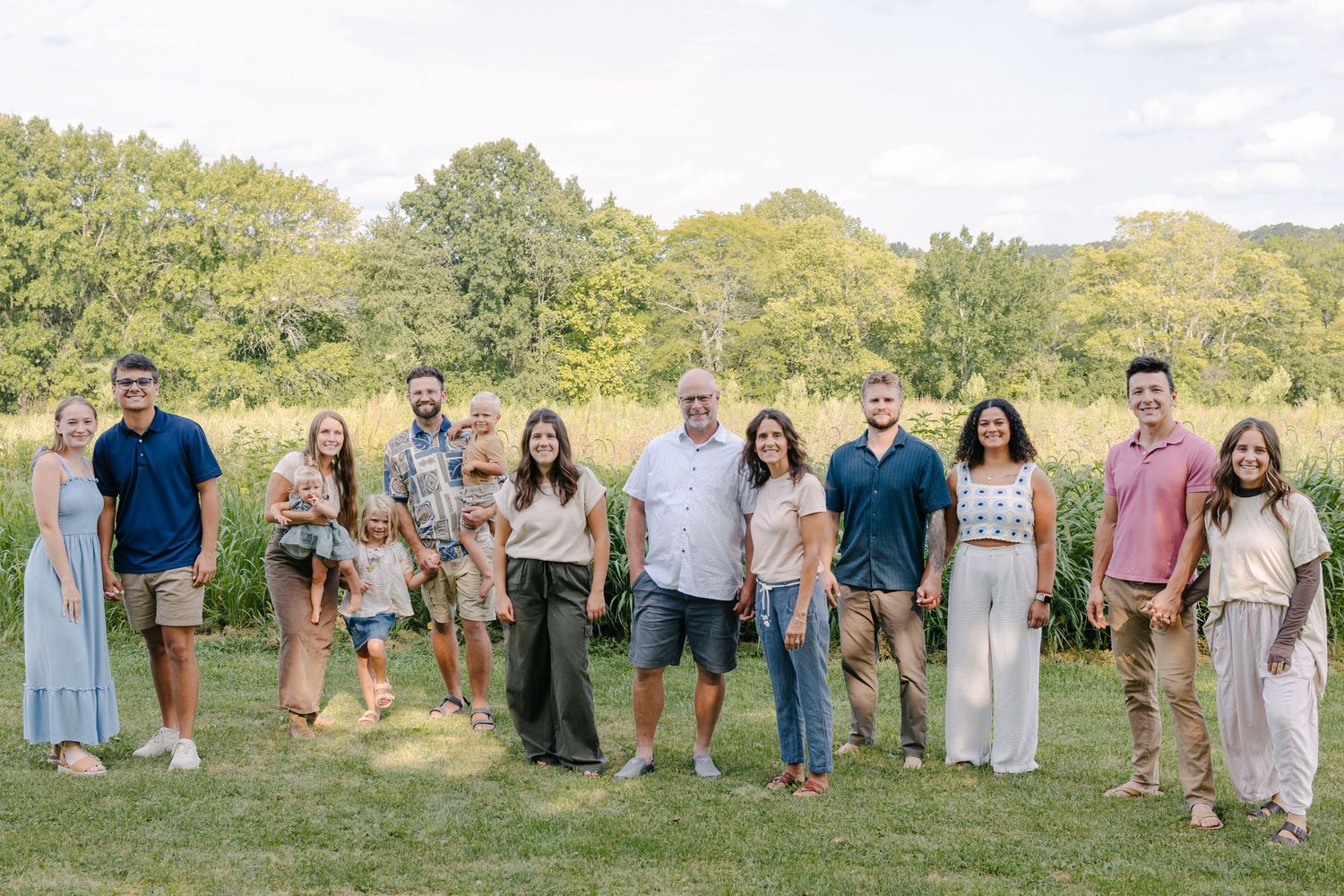 Extended family gathered outdoors for a group portrait in front of a white picket fence and cornfield.