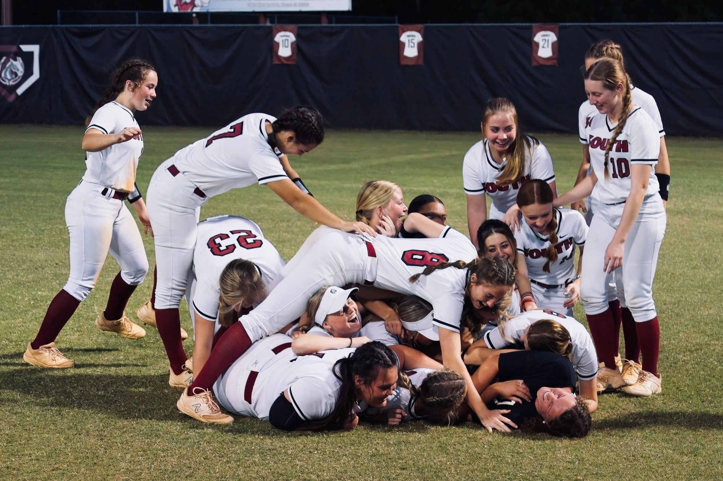 A softball team celebrates victory by piling on top of each other on the field.