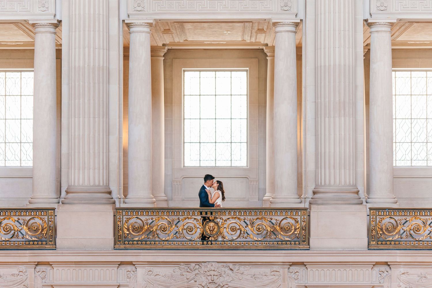 Couple stands on ornate balcony surrounded by classical columns and architecture.