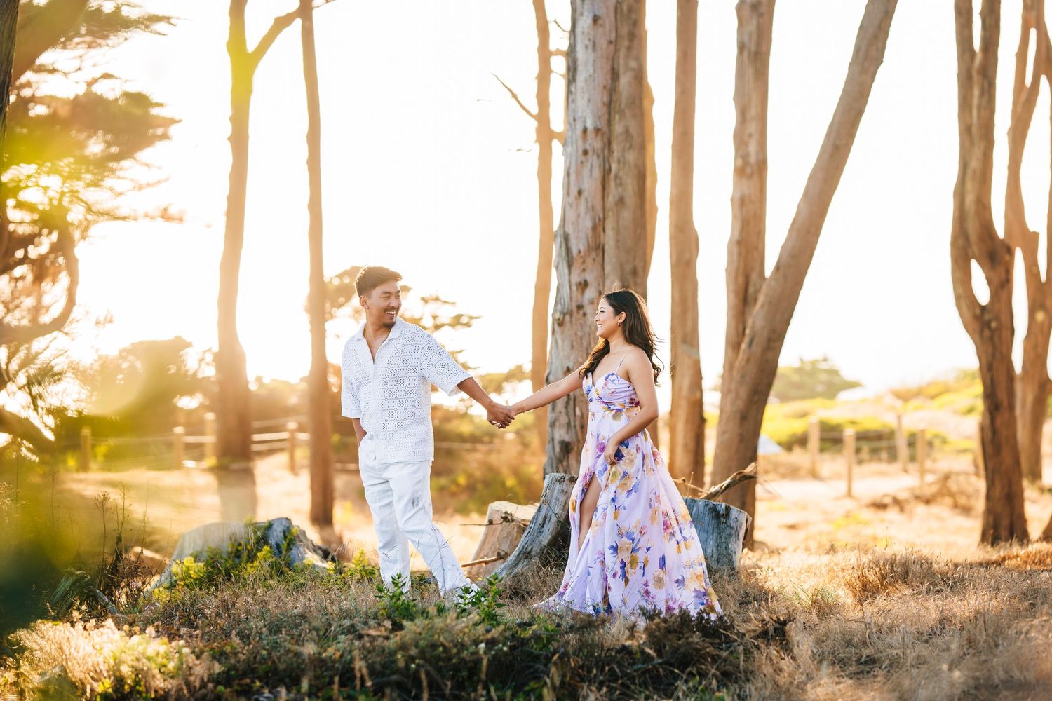 Romantic couple poses among tall trees during golden hour sunset.