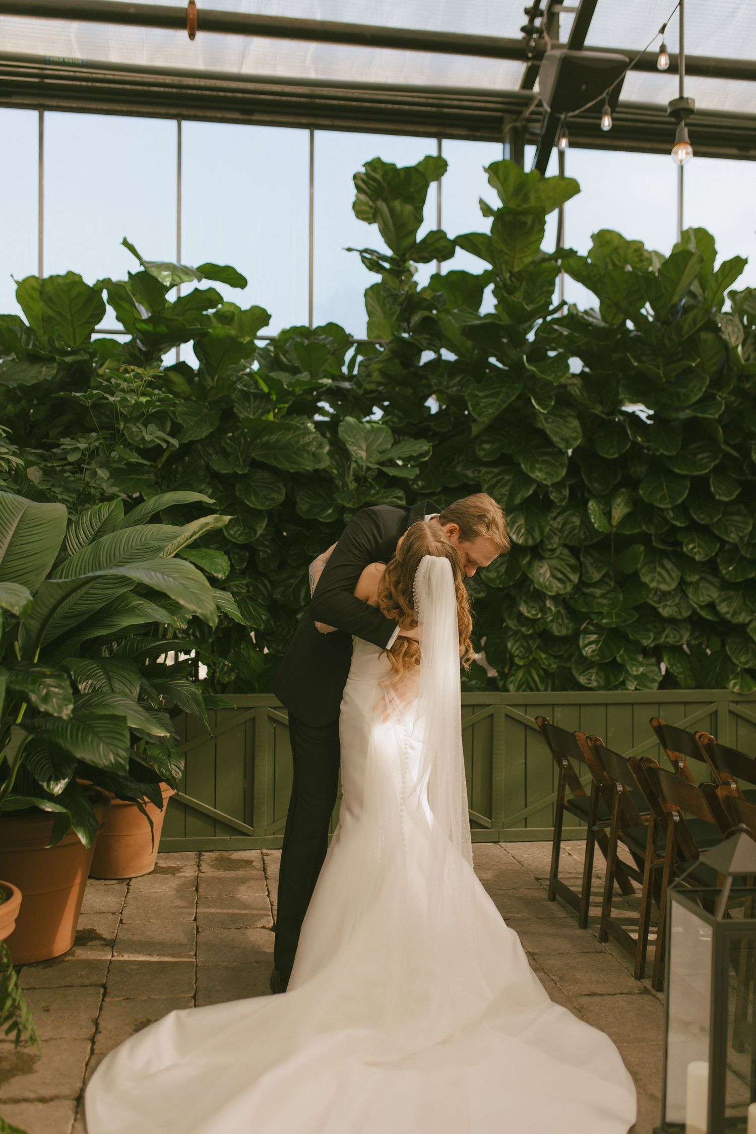 A romantic wedding moment in a greenhouse surrounded by lush greenery.