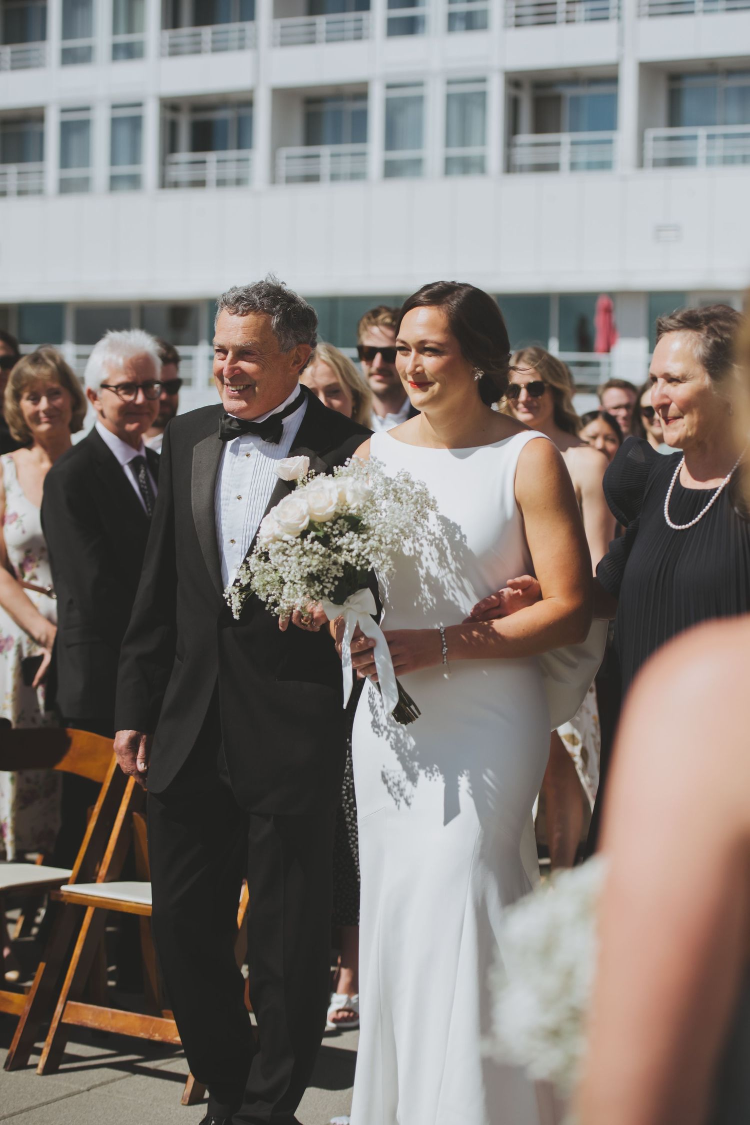 Newlyweds share a joyful moment during outdoor wedding ceremony with a white building in the background.