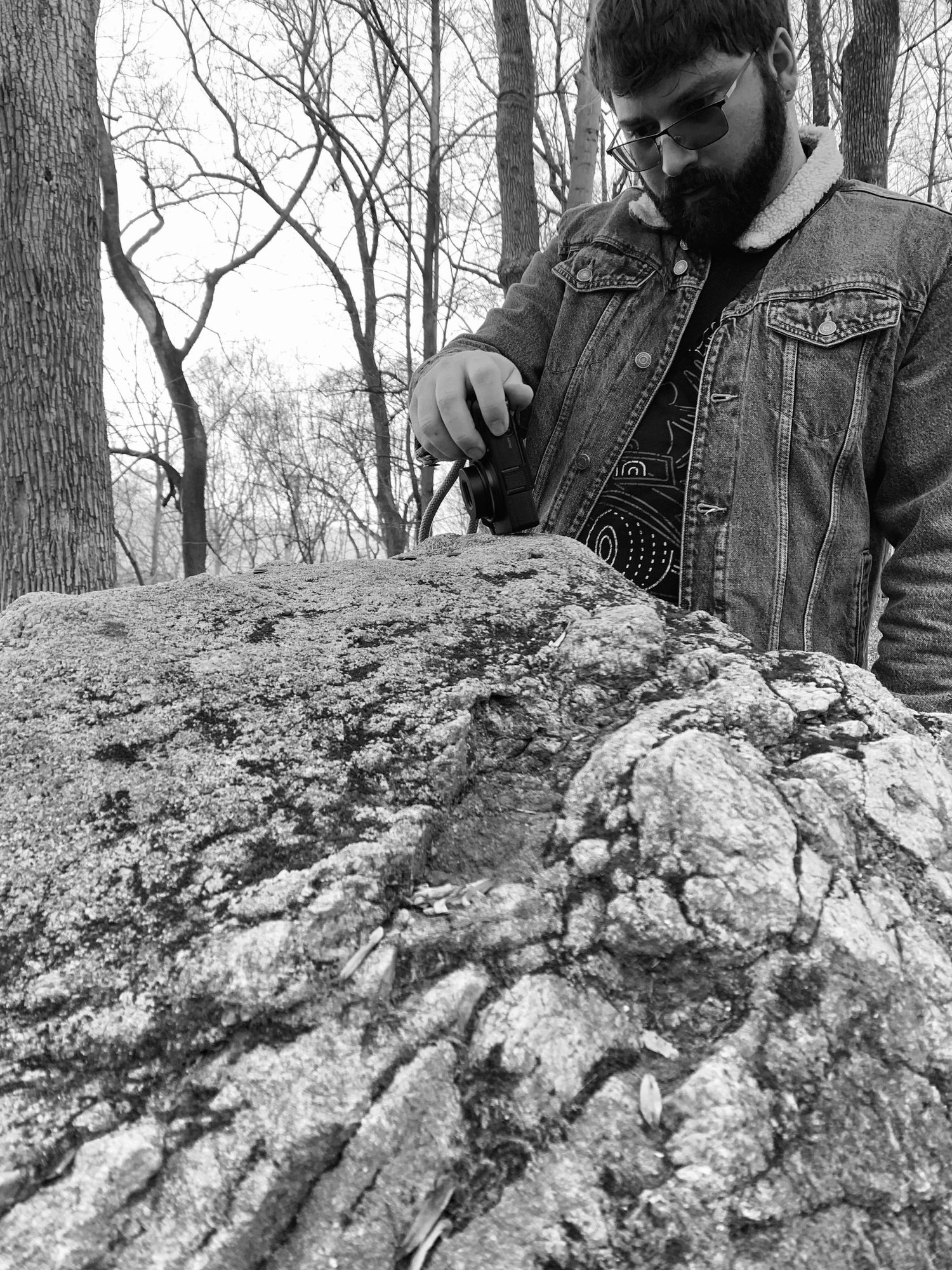 Black and White photo of Ryan (Me) taking a photo of a pile of birdseed a hiker left on a rock. The path led us to this wonderful place.