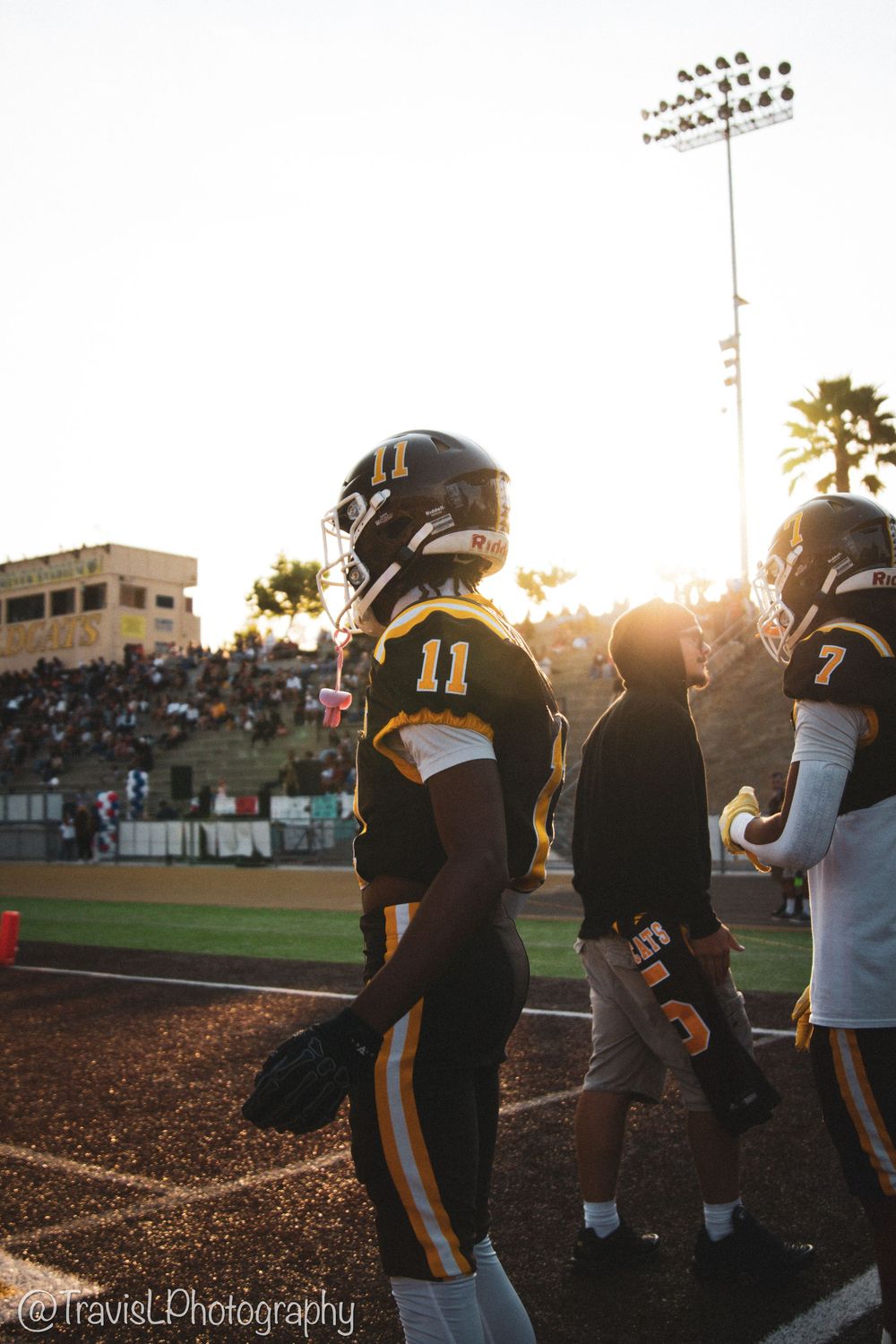 Football team silhouettes against sunset with stadium lights glowing in background.
