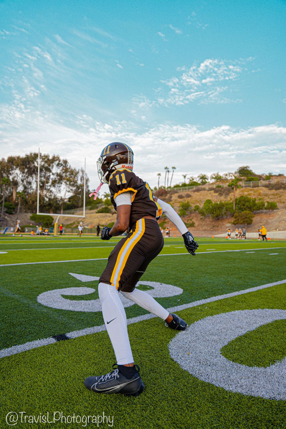 Football player in brown and white uniform crouching on artificial turf field.