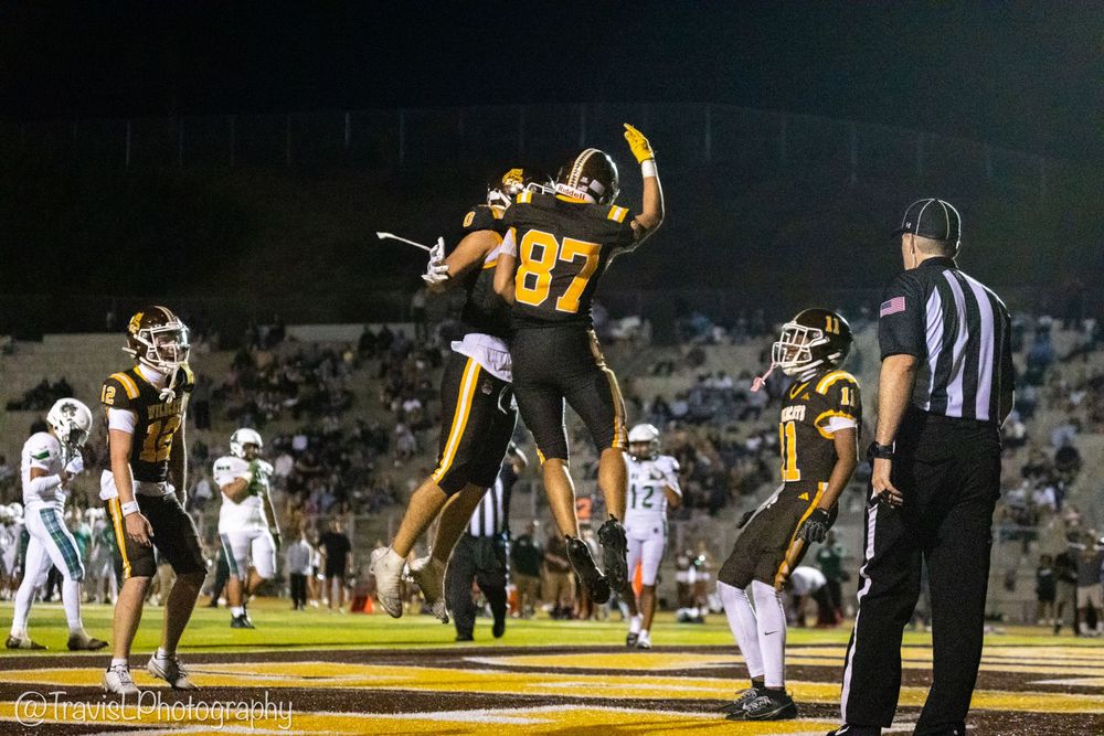 Football players in yellow and white uniforms compete during a nighttime game on an illuminated field.