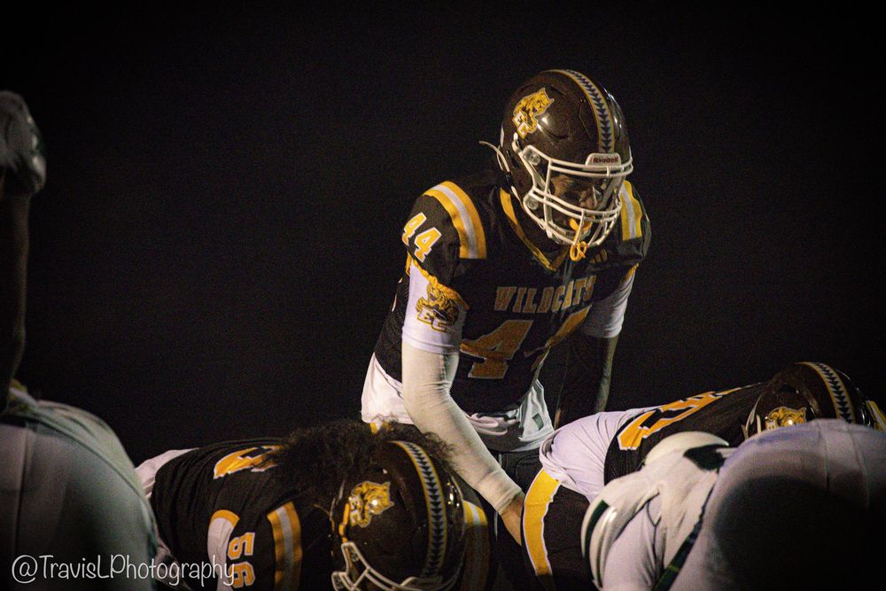 Football teams in yellow and white jerseys prepare for the next play under stadium lights.