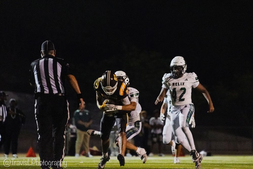 Players from opposing teams clash during a nighttime football game on a lit field.