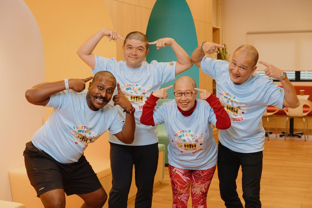 A group of people wearing light blue t-shirts performing choreographed dance moves in a brightly lit room.