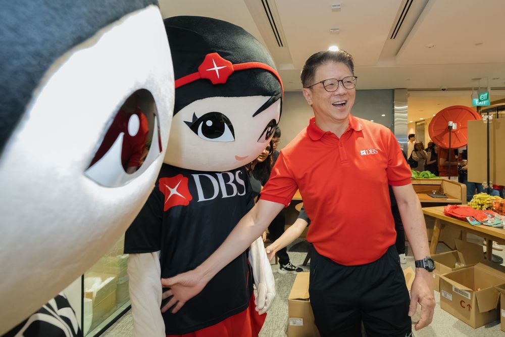 A person in red attire and others pose with a large plush whale mascot at a shopping center.