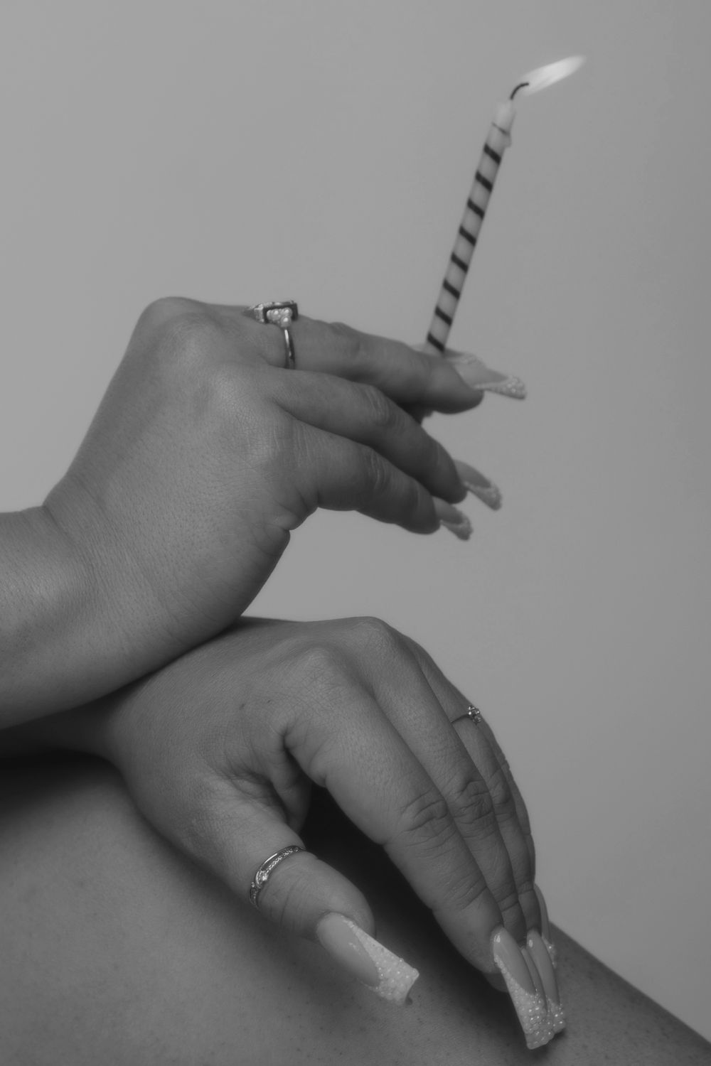 Close-up of manicured hands with rings holding a striped birthday candle.