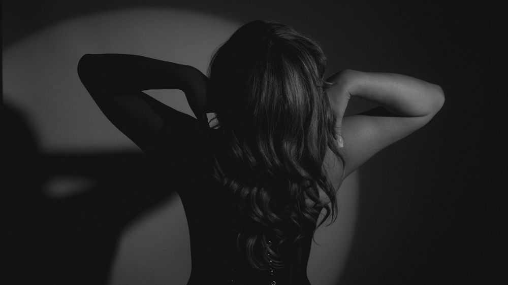 Silhouette of person with long wavy hair from behind in dark moody lighting.