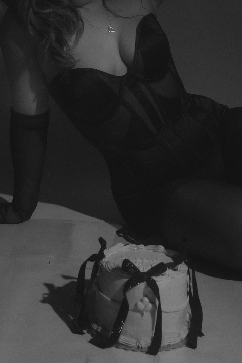 Dramatic black and white photo of person in black dress next to decorated cake.