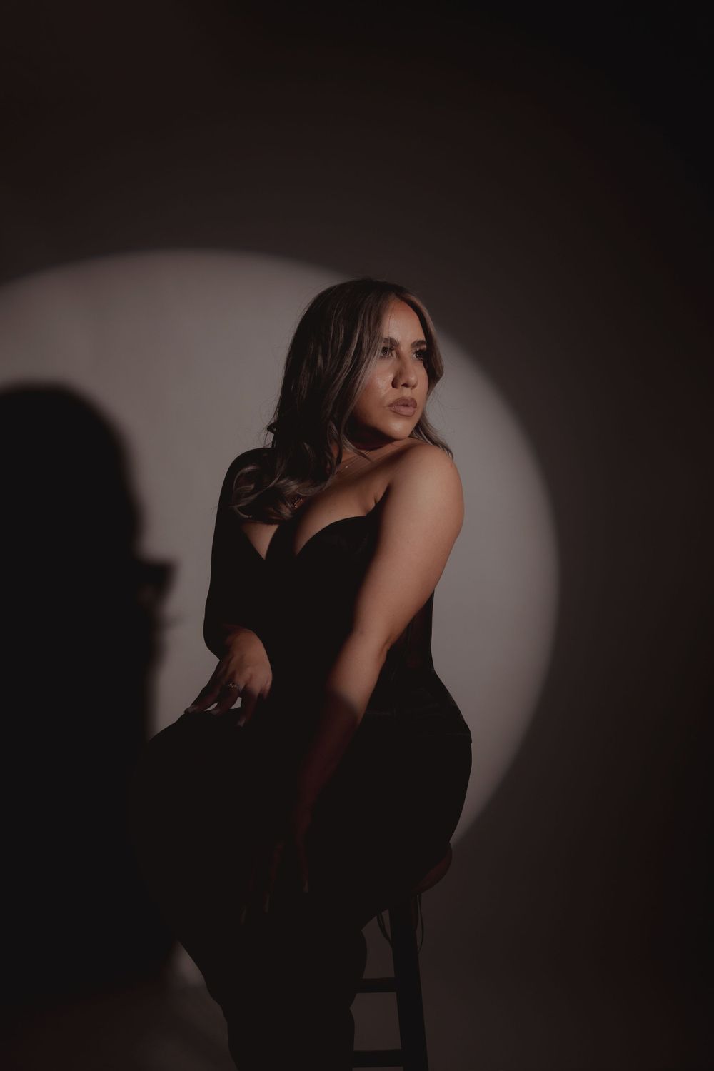Dramatic portrait in black dress against dark background with spotlight creating atmospheric shadows.