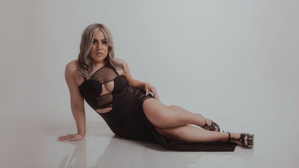 Glamour portrait with subject reclining in black dress against white background.